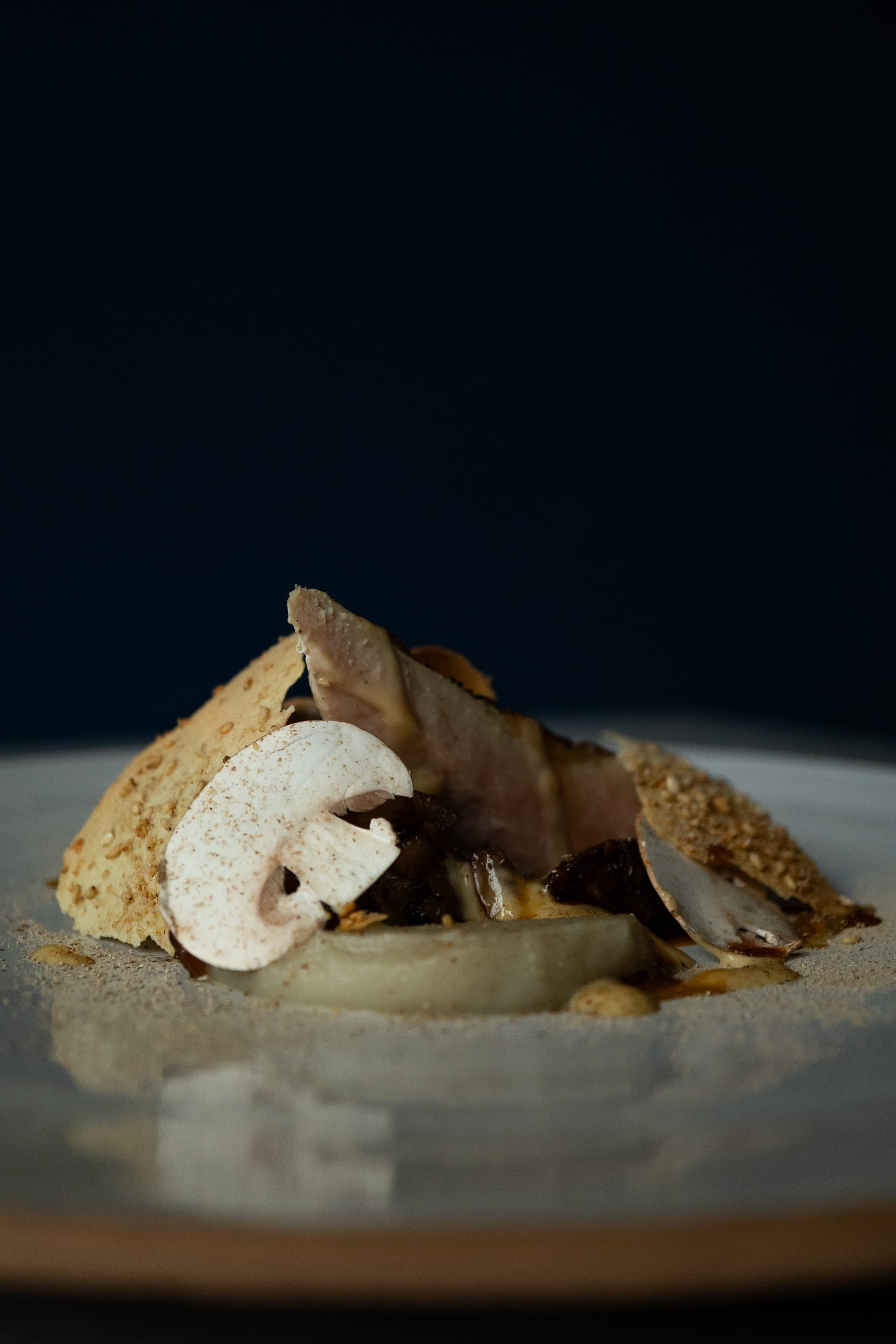 Plat dressé avec lamelle de champignon, tuile croustillante, sur fond bleu nuit