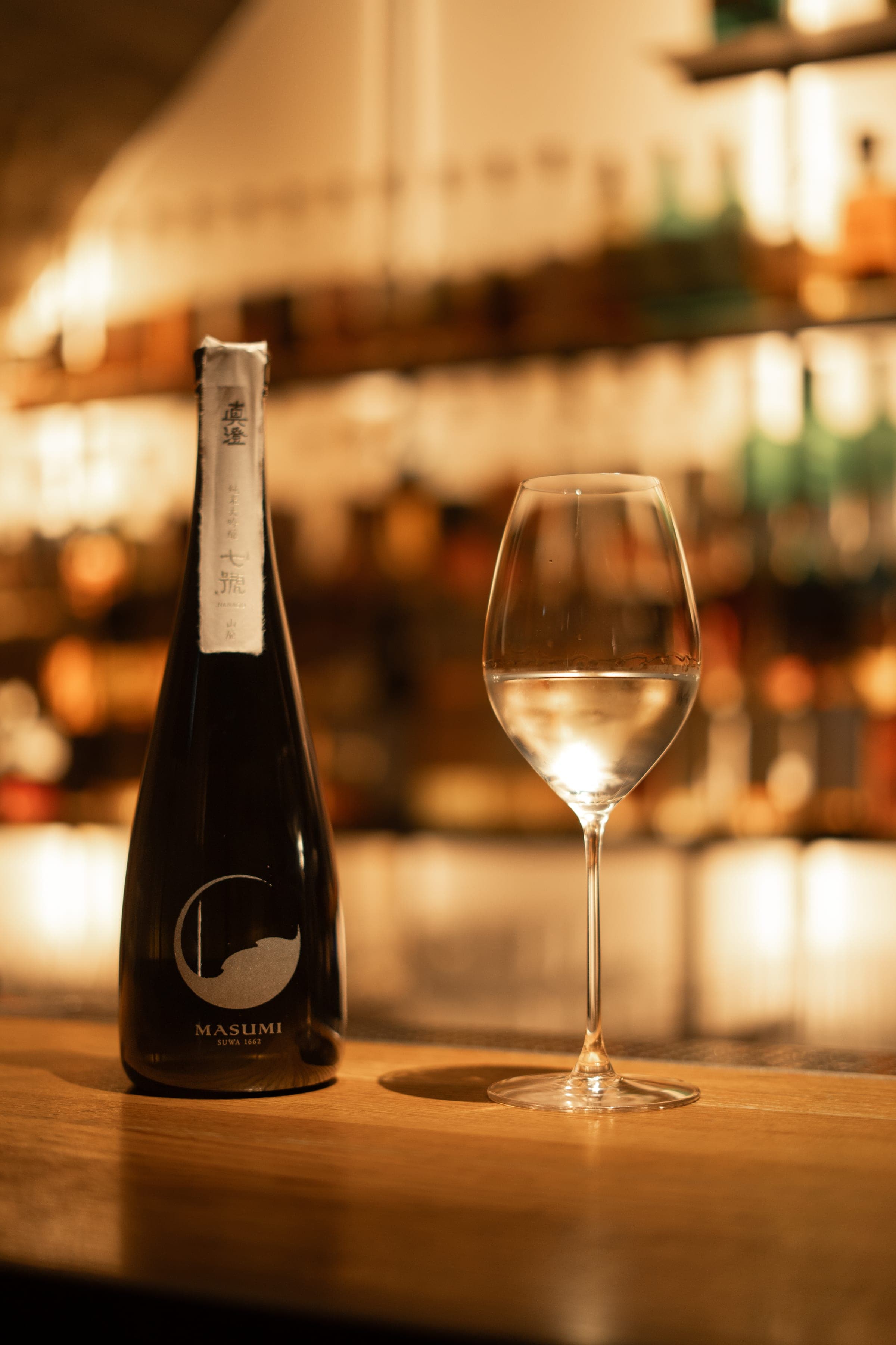 Bouteille de saké et verre à vin sur le comptoir du bar, étagères en arrière-plan