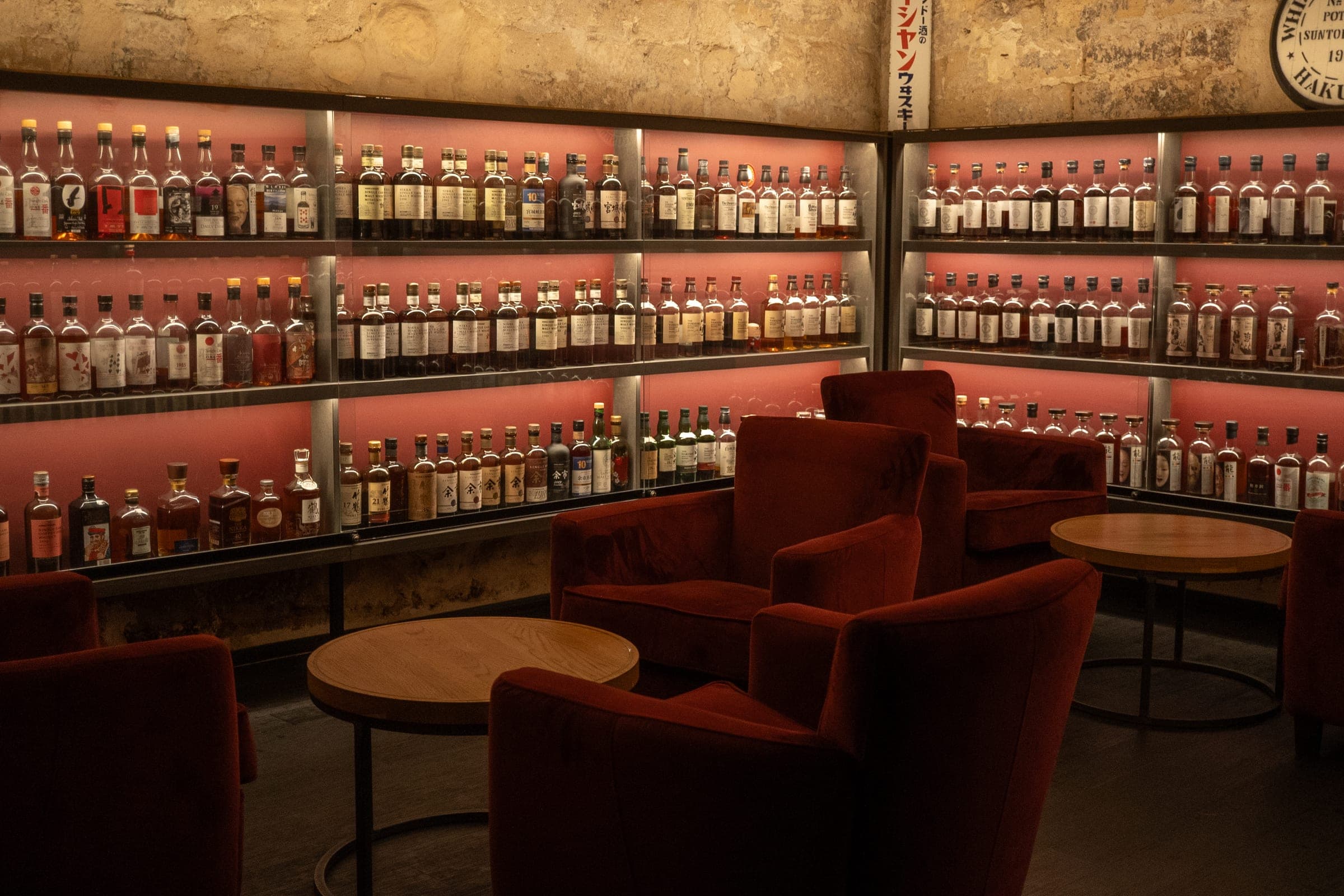 Salon aux fauteuils de velours rouge, face au mur de whiskies