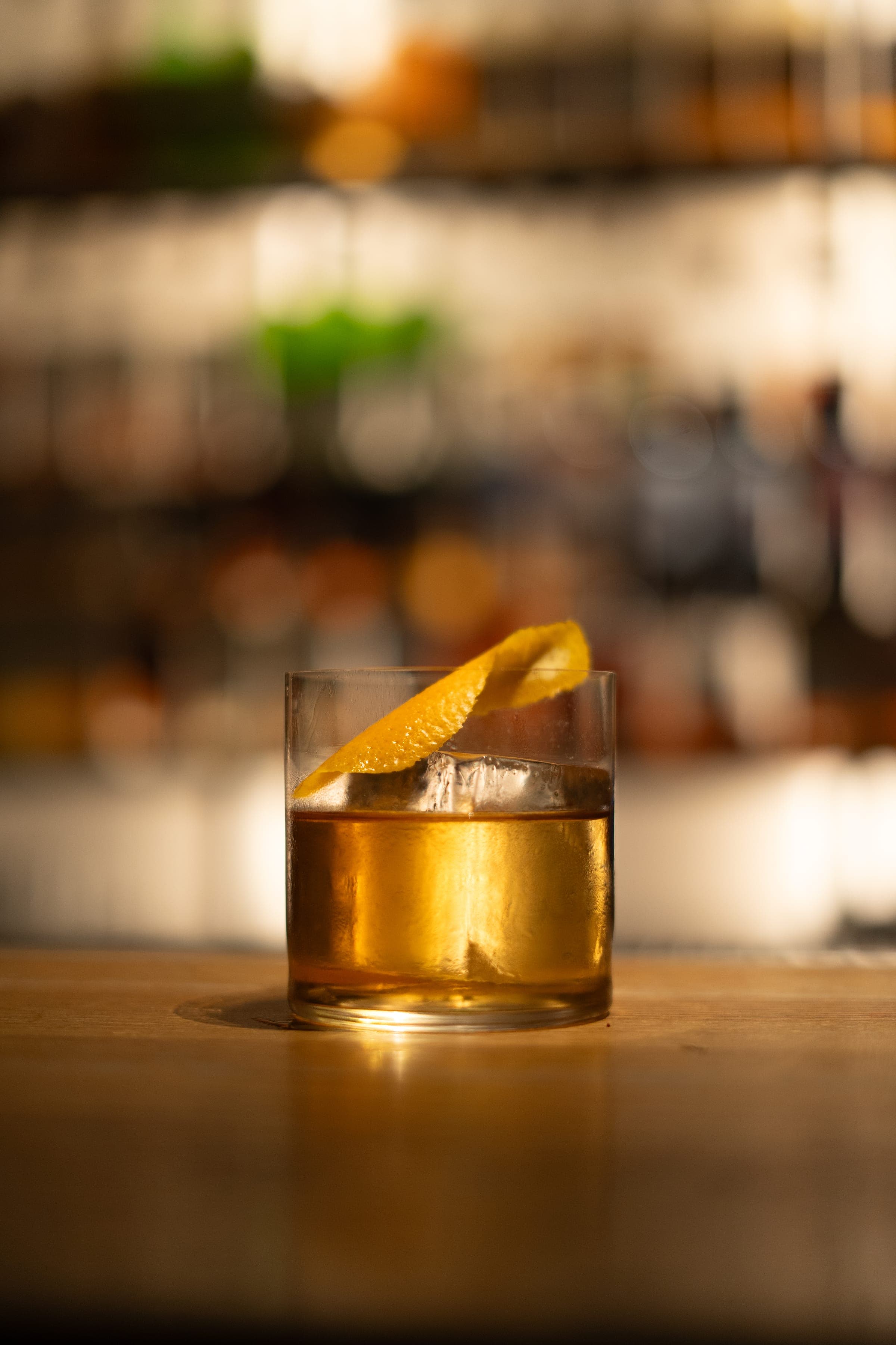 Cocktail ambré garni d'un zeste d'orange, sur le comptoir du bar