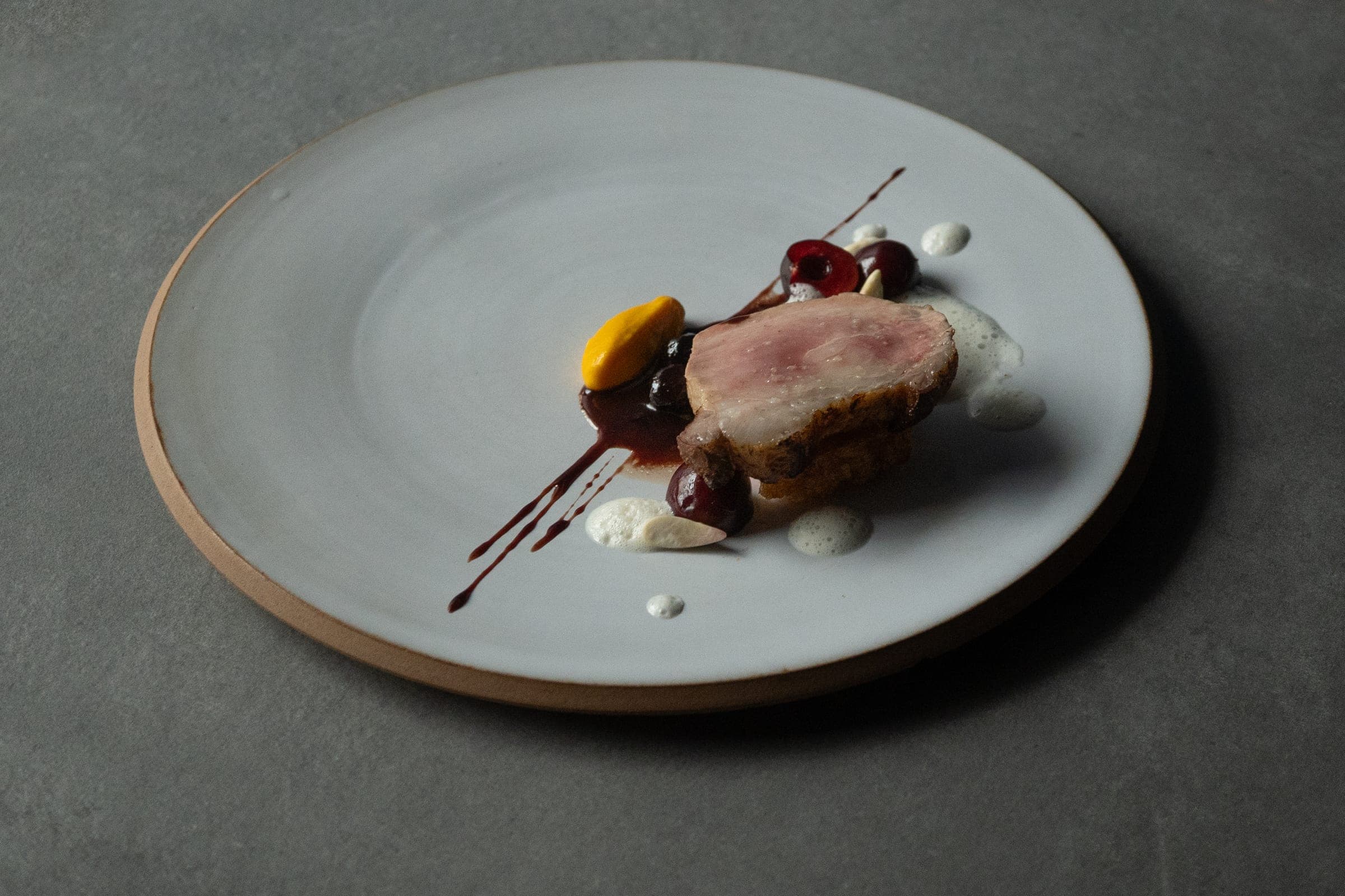 Pièce de viande rosée en dressage épuré, cerises et sauce chocolatée, dressage épuré sur assiette blanche